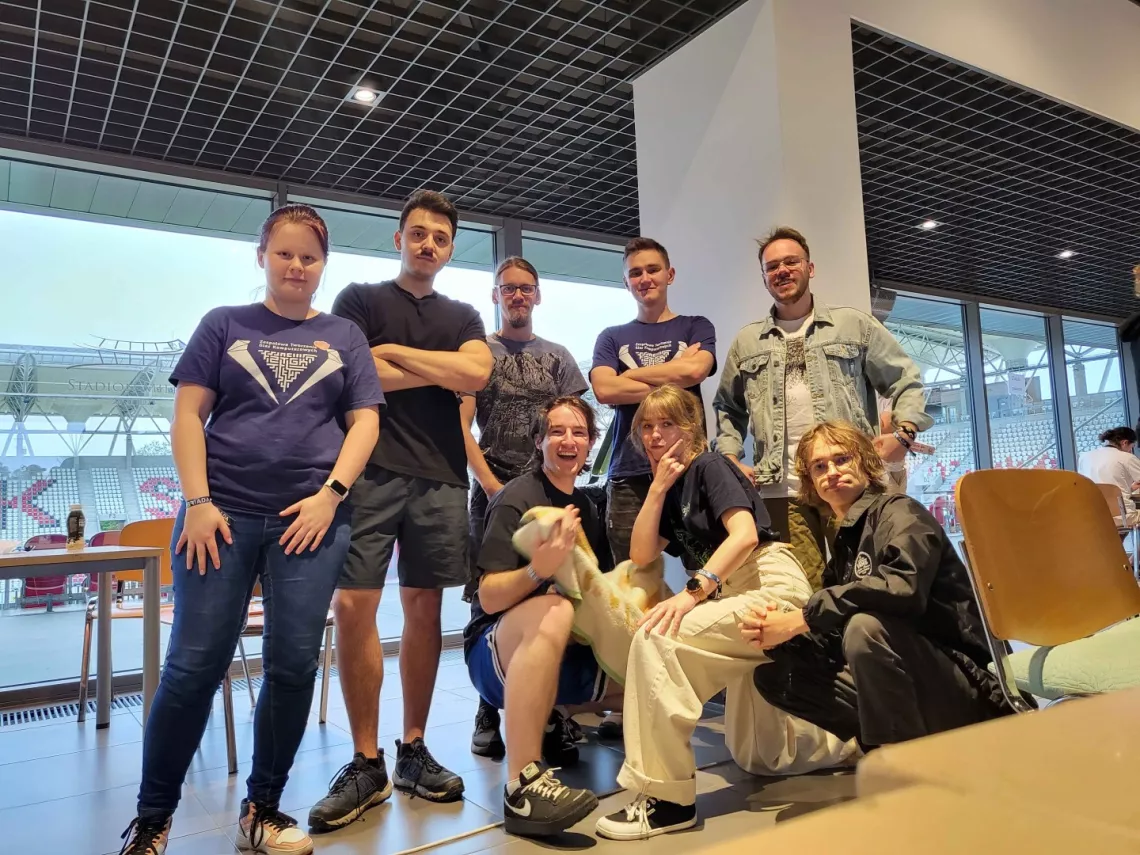 Drużyna Gleaming Geckos - ośmioro młodych ludzi stoi na tle przeszklonej ściany 