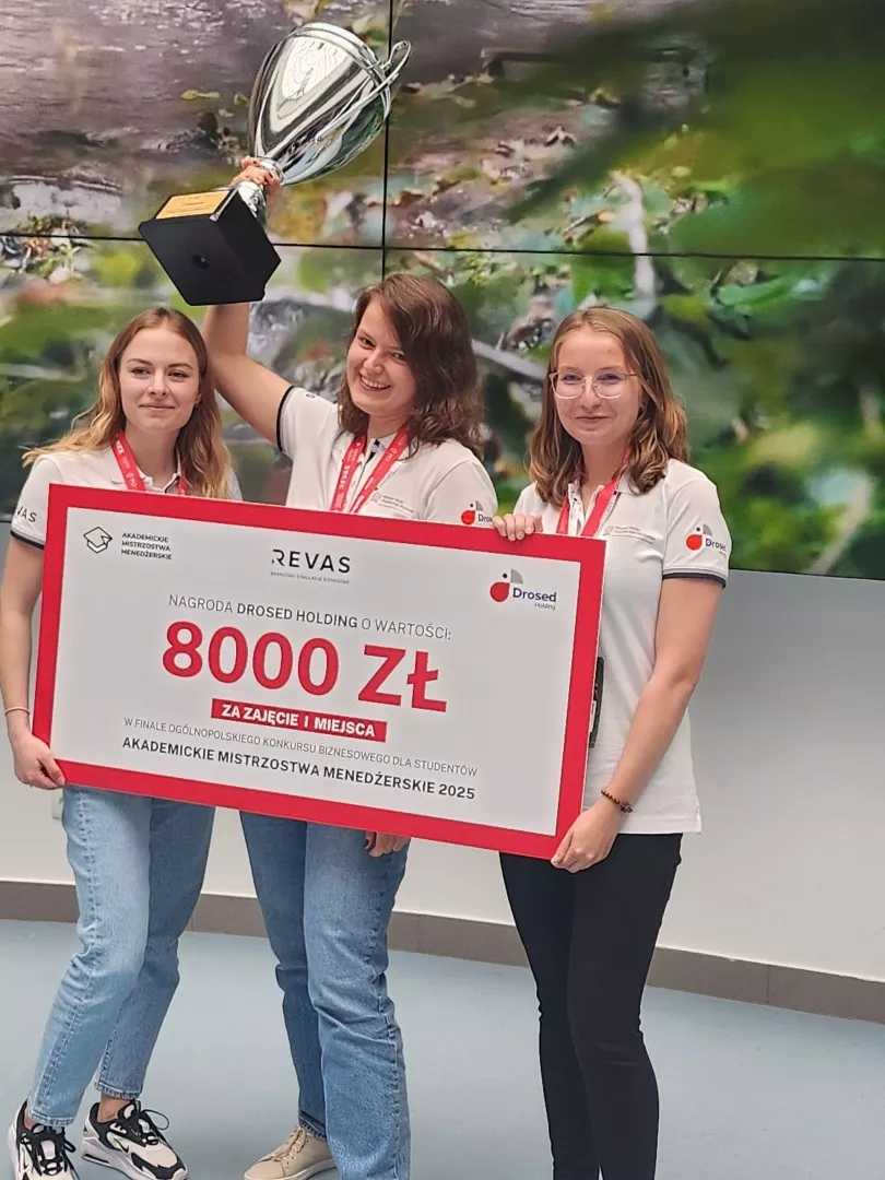 Trzy osoby stoją, trzymając puchar i symboliczny czek na kwotę 8000 zł