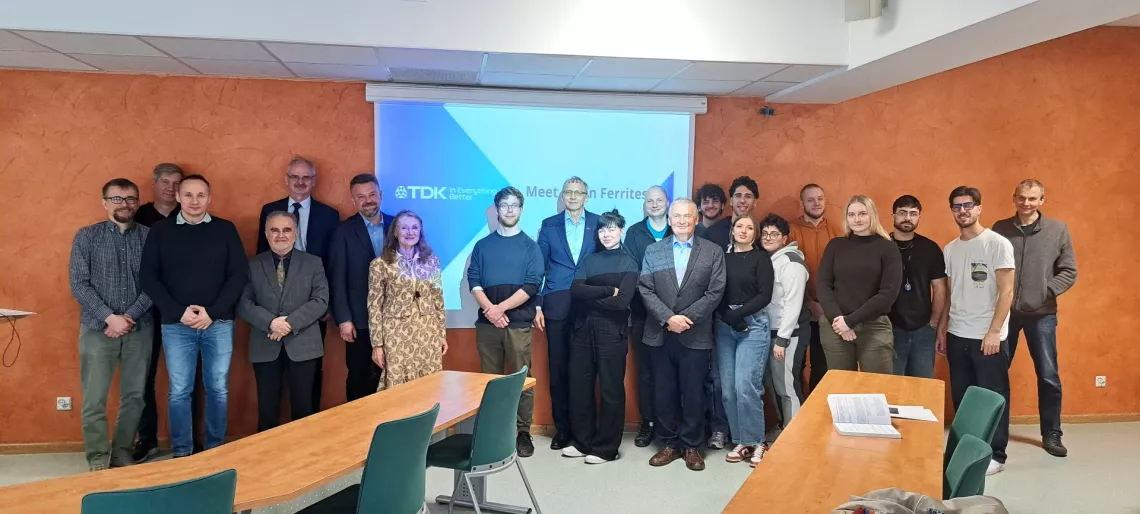 Kilkanaście osób stoi w sali seminaryjnej na tle ekranu wyświetlającego nazwę firmy TDK i tytuł spotkania Meet MnZn Ferrites 