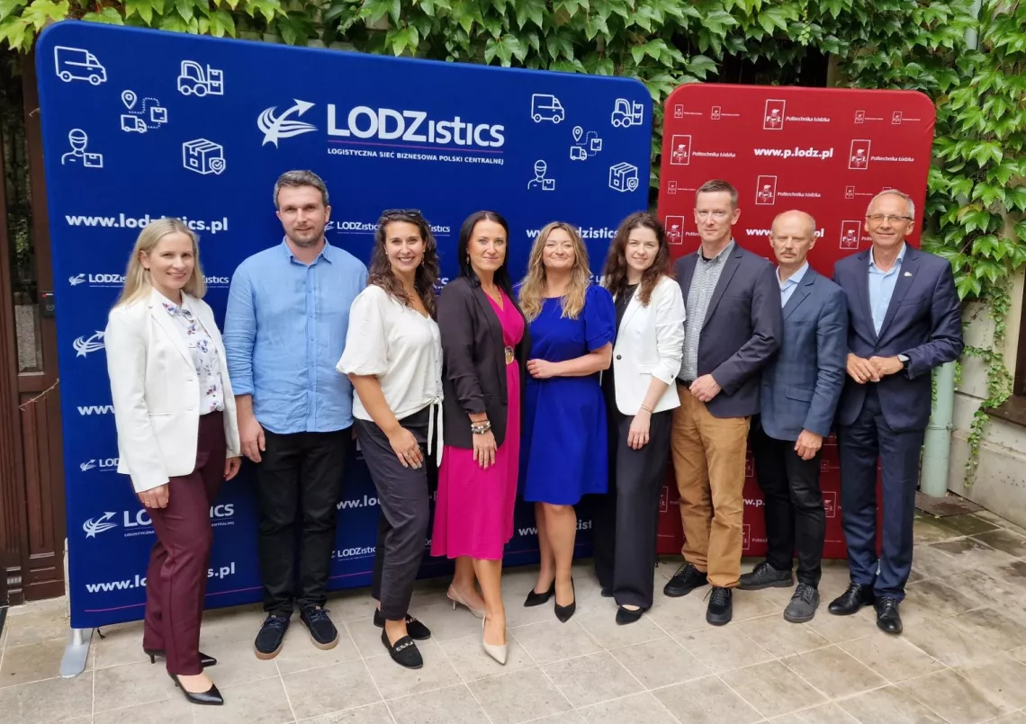 Dziewięć osob stoi na tle banerów z napisem LODZistics i Politechnika Łódzka