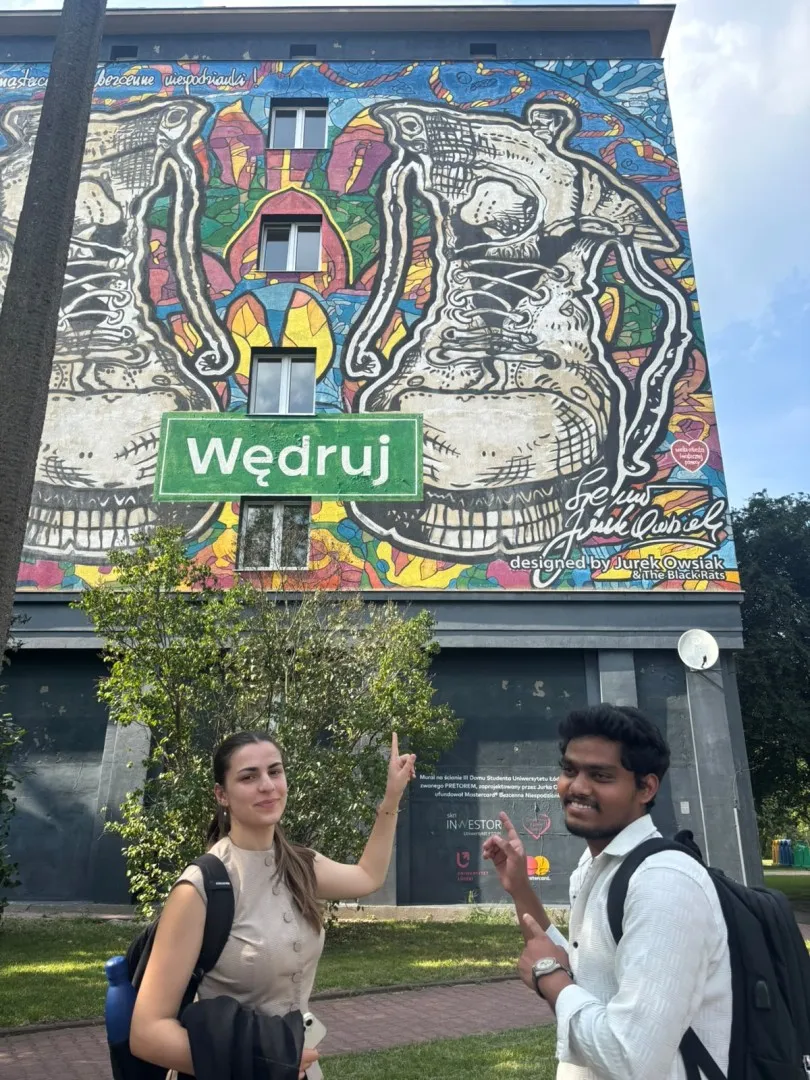 Dwoje studentów stoi pod muralem namalowanym na szczytowej ścianieamienicy