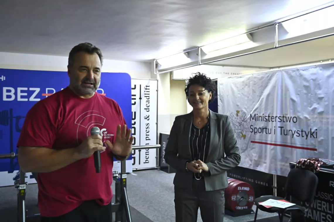 Kobieta w garniturze i mężczyzna w podkoszulce, który przemawia do mikrofonu