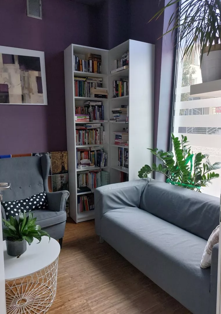 Pomieszczenie, w którym stoi regał z ksiązkami, sofa, fotel i podręczny stolik