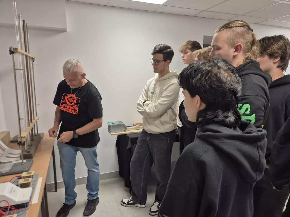 Prowadzący zajęcia prezentuje doświadczenie fizyczne, które obseruje grupa uczniów