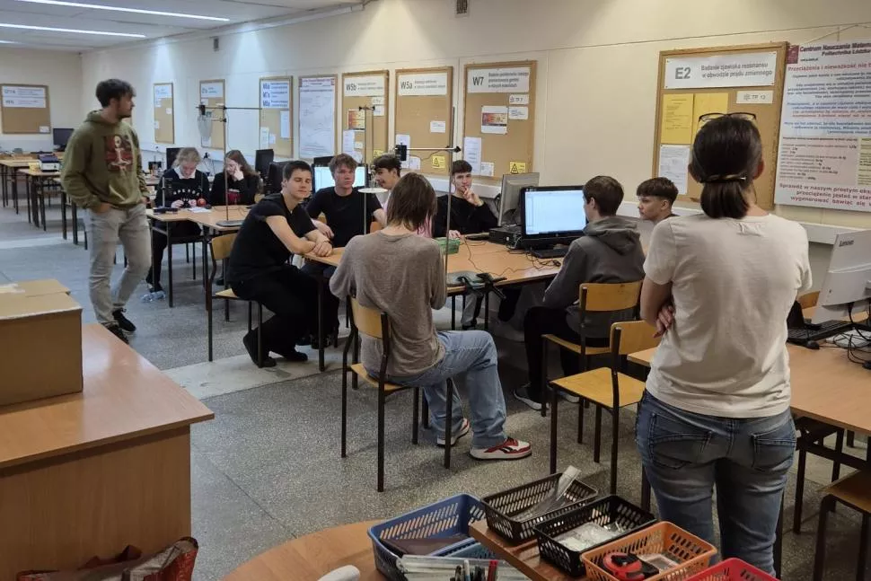 Młodzież w czasie zajęć w sali seminaryjej, siedzi pzry stołach, na których stoja komputery. Na ścianach wiszą tablice z różnymi informacjami