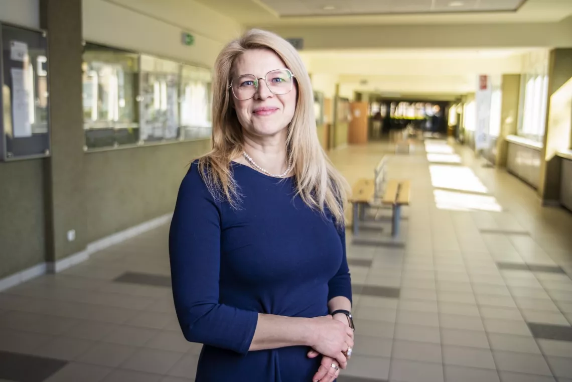 Kobieta stoi w korytarzu, po prawej widać okna, po lewej gabloty.