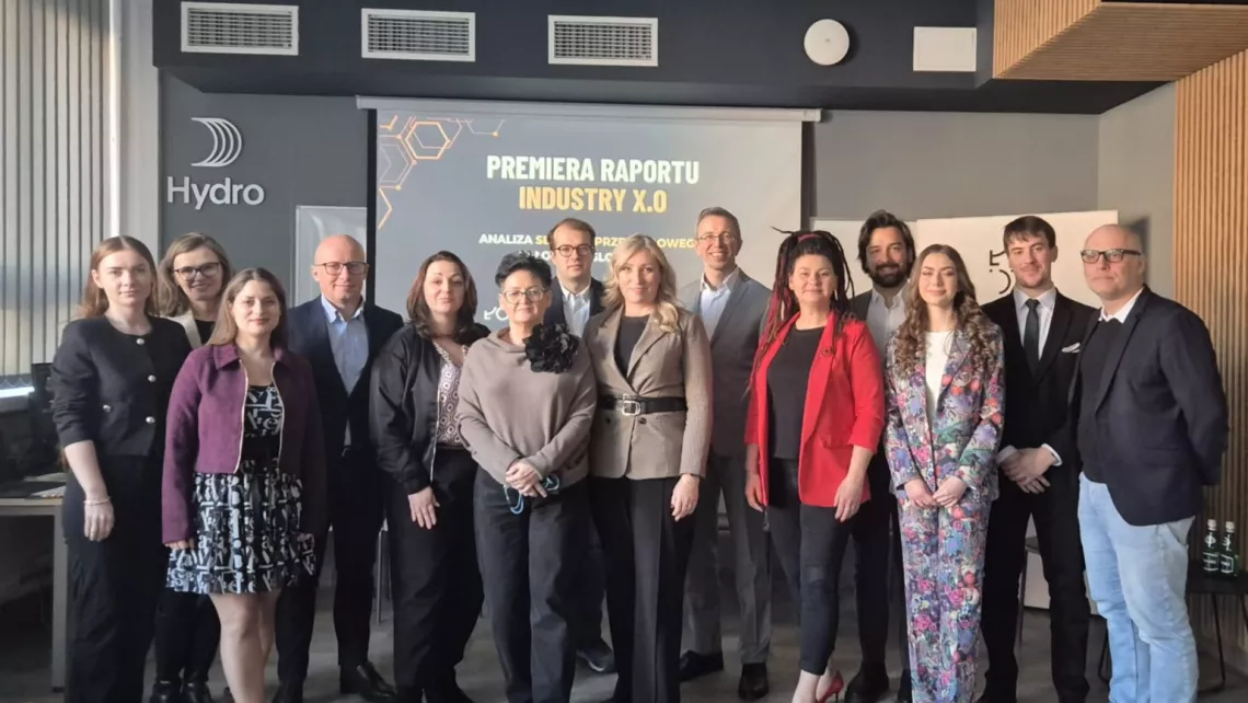 Grupa osób stoi na tle ekranu z napisem Premiera raportu Industry X.0