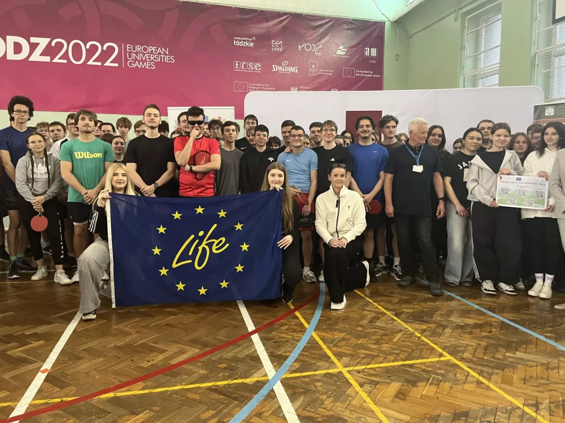 Grupa sportowo ubranych osób stoi, a dwie z nich trzymają flagę z napisem life
