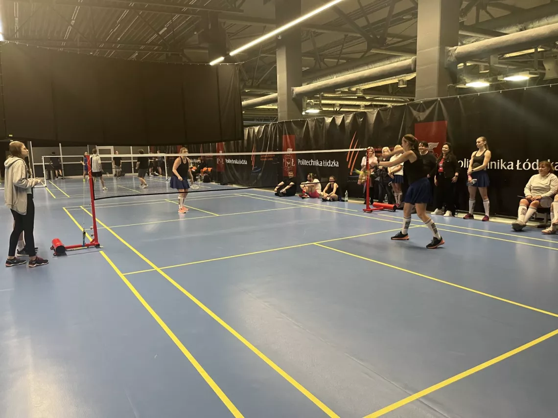 Zawodnicy i zawodniczki grają w badmintona na dwóch boiskach.