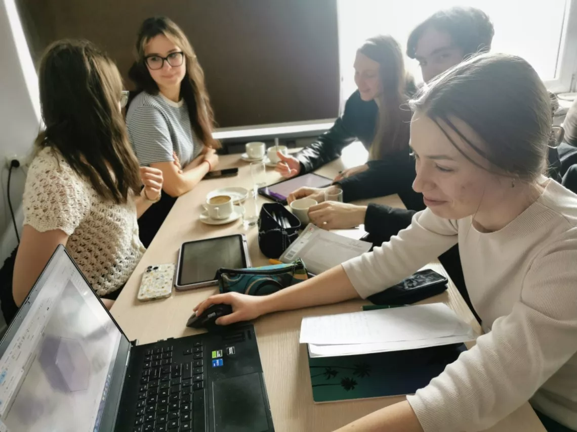 Kilka młodych osób siedzi, pracując przy laptopach i tabletach