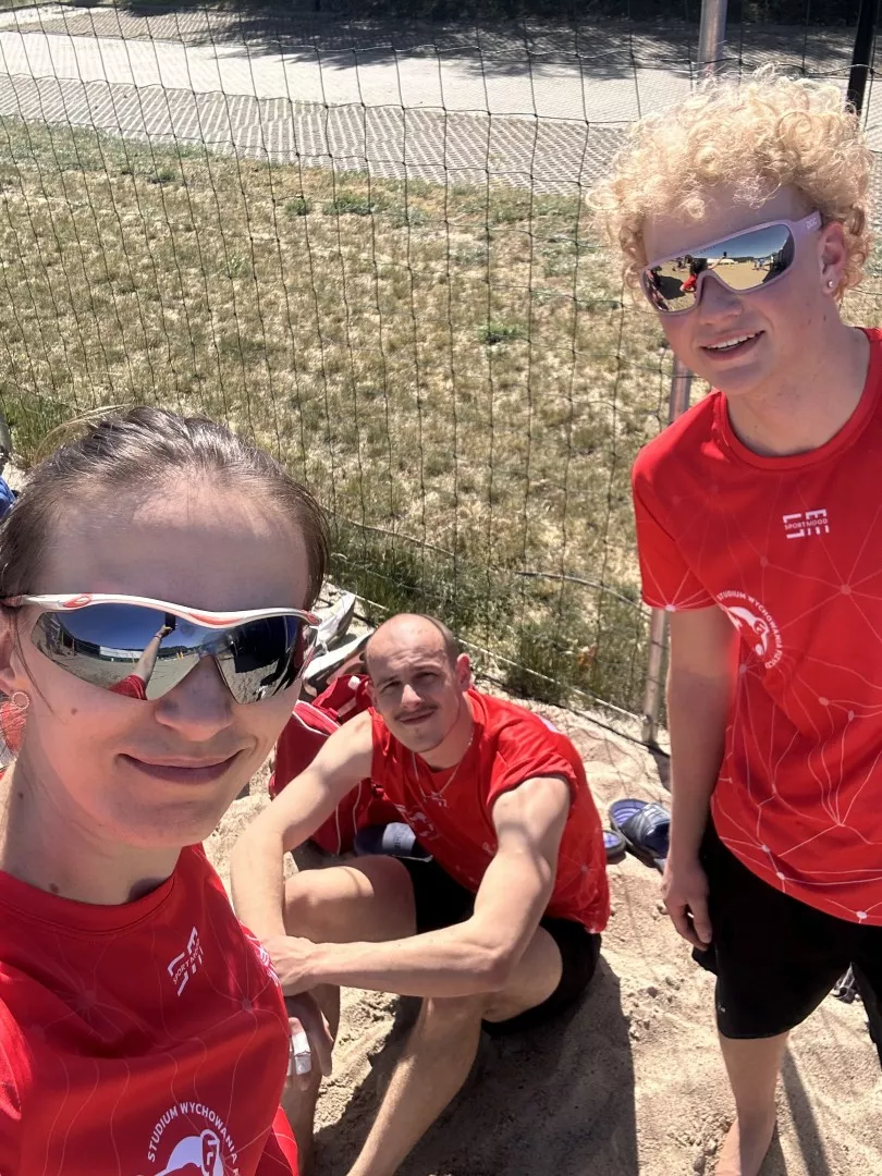 Trzy osoby w sportowych koszulkach na boisku do piłki plażowej