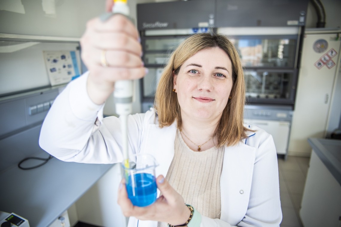 Badaczka w laboratorium trzyma w dłoniach szklane naczynie i przyrząd pomiarowy