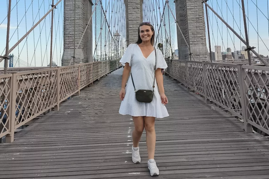 Młoda uśmiechnięta kobieta w białej sukience stoi na moście.
