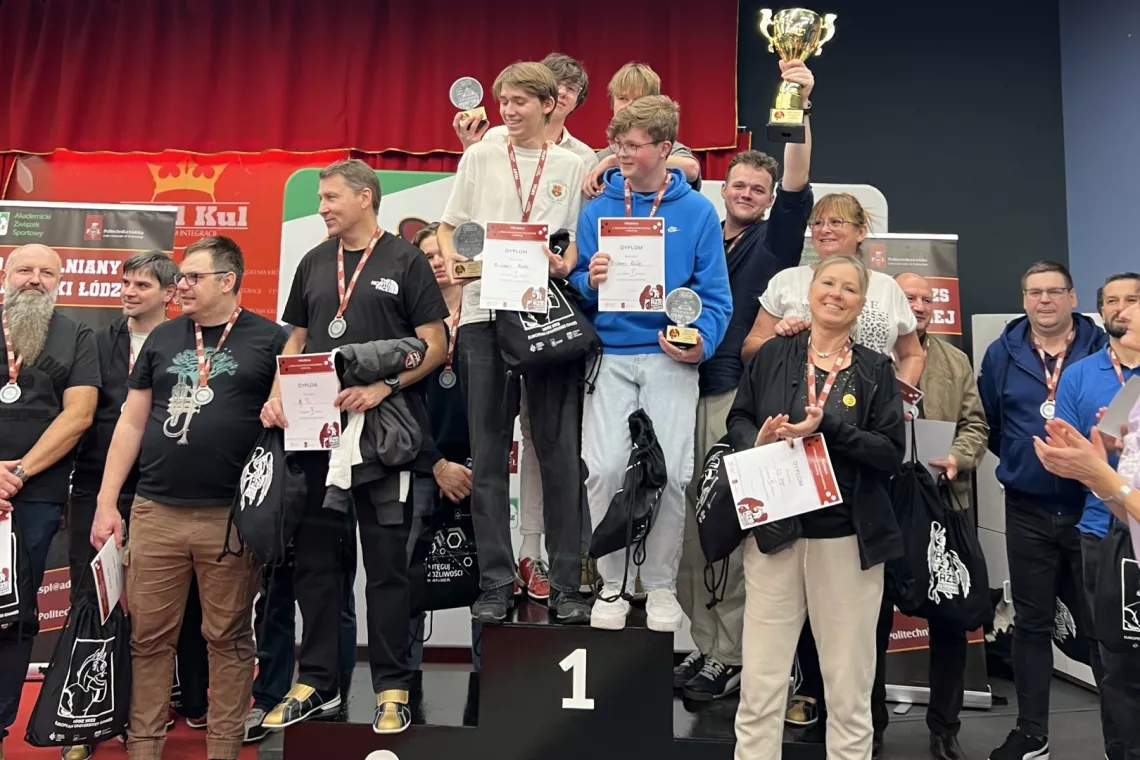 Liczna grupa z dyplomami w rekach i pucharem stoi na stopniach podium