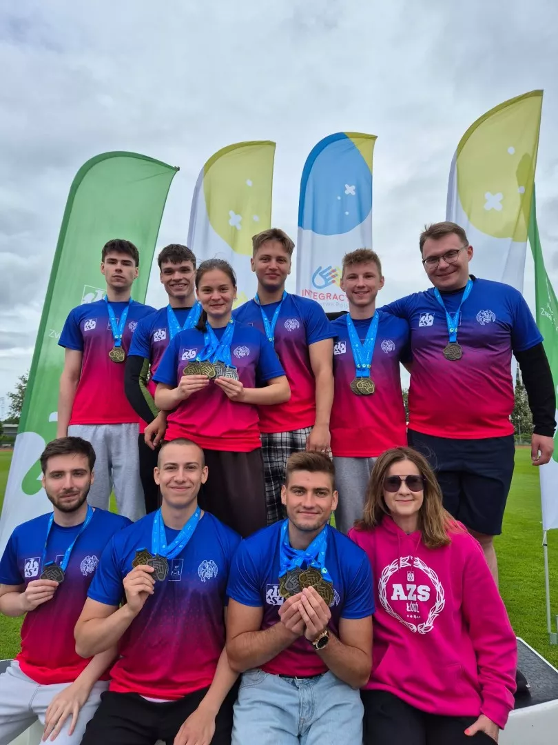 Grupa sportowców lekkoatletów prezentuje medale, stojąc w dwóch rzędach na tle winderów