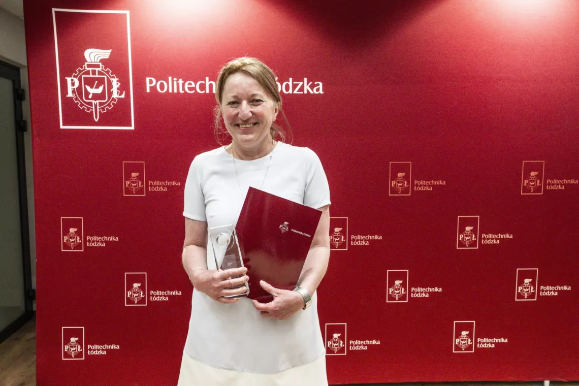 Uśmiechnięta kobieta ze statuetką, w tle ścianka z napisem Politechnika Łódzka