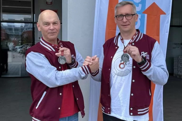Dwaj mężczyżni w bordowo-szarych bluzach prezentuja medale zawieszone na szyi.