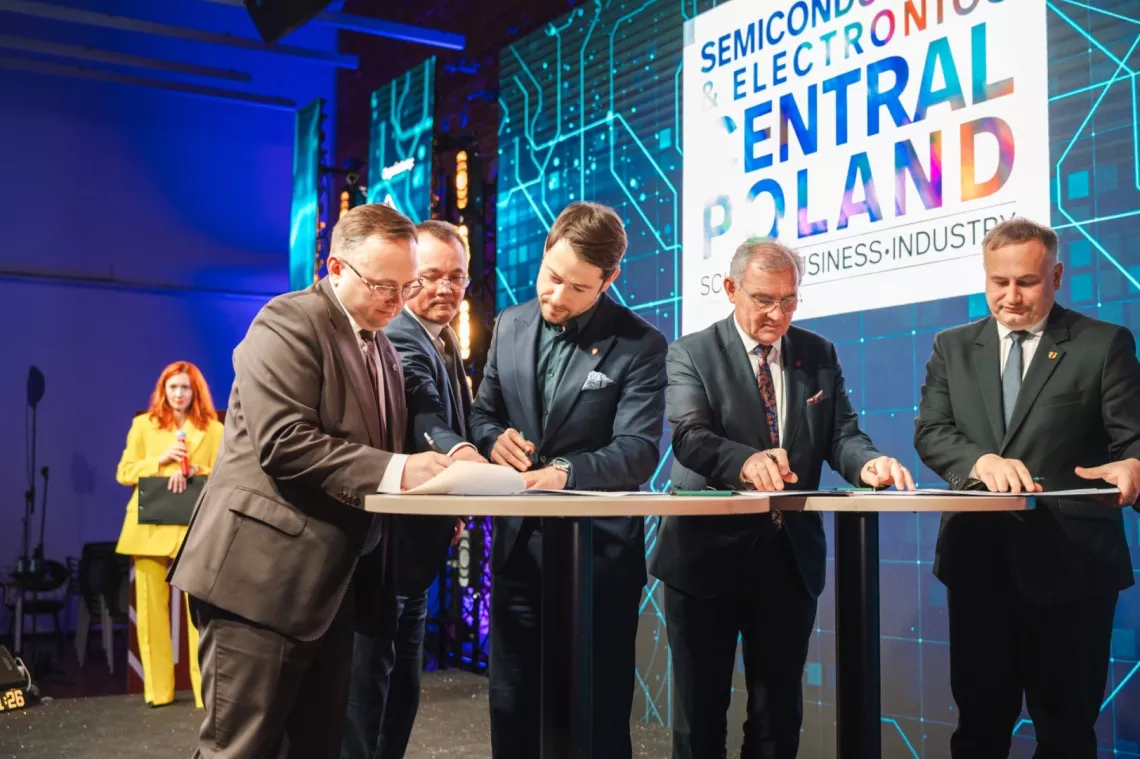 Sygnatariusze podpisujący na stojąco list intencyjny. Z tyłu wyświetla się ekran z nazwą konferencji