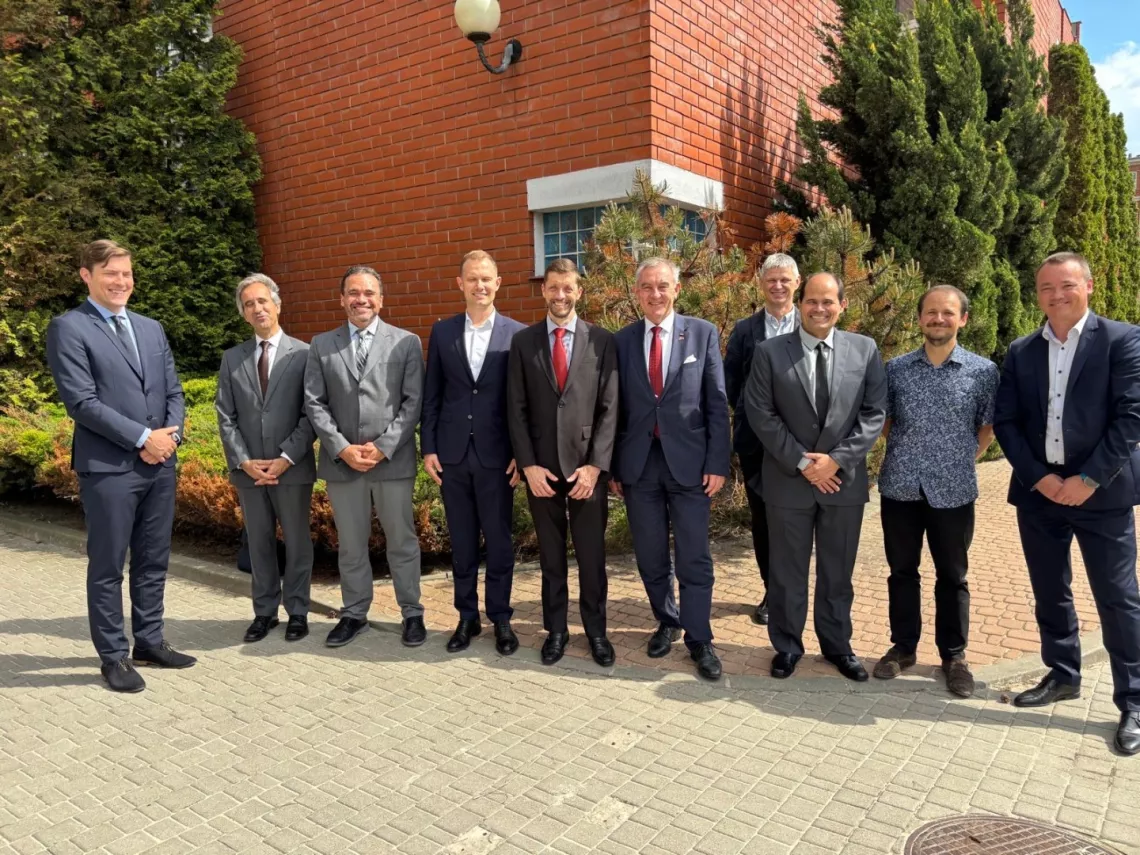 Dziesięcioro mężczyzn stoi na tle budynku z czerwonej cegły otoczonego zielenią