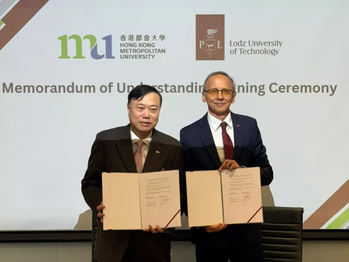 Dwóch mężczyzn trzyma w rękach podpisaną umowę, z tyłu wyświetla się slajd z logo obu uczelni