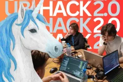 jednorożec, a za nim studenci pracujący przy laptopach i naspi UBIHACK 2.0