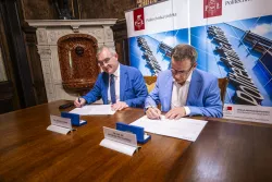 Dokument podpisuje dówch mężczyzn. W tle rollupy z napisem Politechnika Łódzkaali oraz elementy historycznego wystroju pomieszczenia