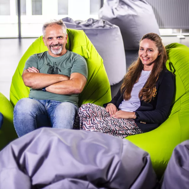 Troje usmiechniętych osób, dwie kobiety i mężczyzna w środku, siedzi na pufach