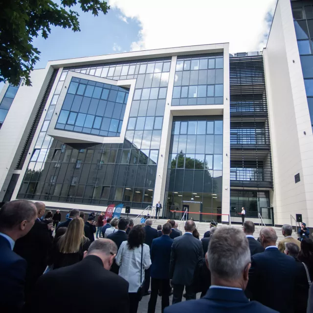 Nowoczesny, przeszklony budynek, przed którym stoi licznie zgromadzona  publiczność