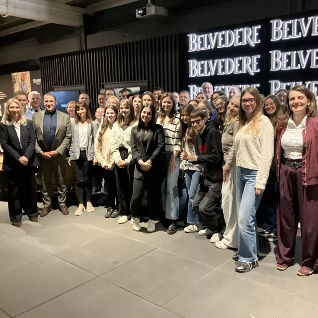 Grupa osób stoi na tle ściany z napisem Belvedere