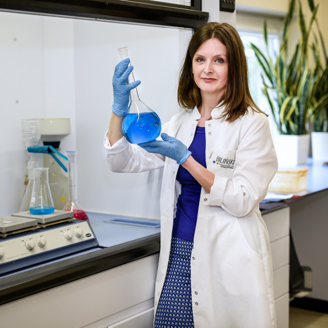 Dr inz. Lucyna Bilińska trzyma w ręku szklane naczynie z niebieską cieczą